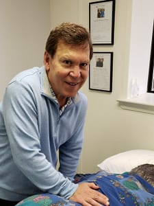 Tom looks up and smiles while working on lower back of patient